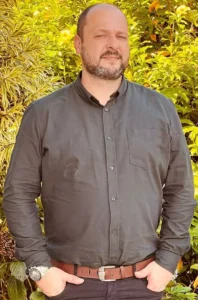 homem branco e calvo vestindo camisa e calça social de cor cinza escuro